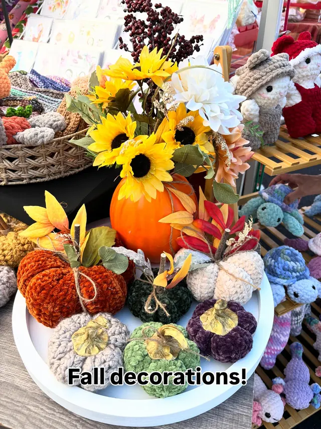 Crochet fall pumpkins in rust, cream, green, purple and grey on a white tray, with sunflowers and crochet animals around them.